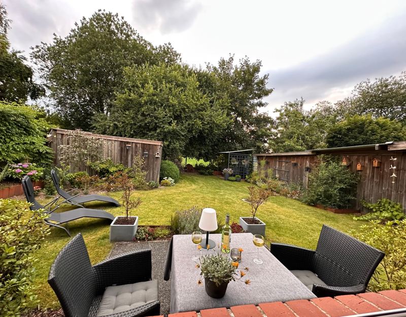 Terrasse mit Tisch und Stühlen und Blick in den Garten mit Sonnenliegen
