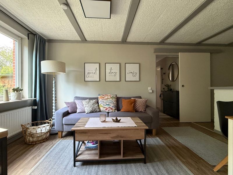 Wohnbereich mit Sofa, Couchtisch aus Holz, Stehlampe und Fenster zum Garten