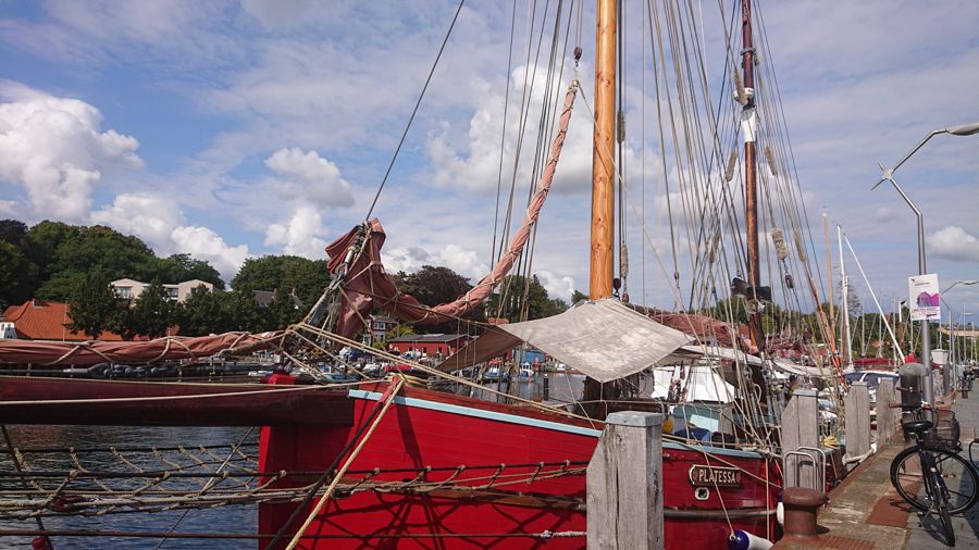 Roter Traditionssegler im Hafen an der Ostsee unter Sommerwolken